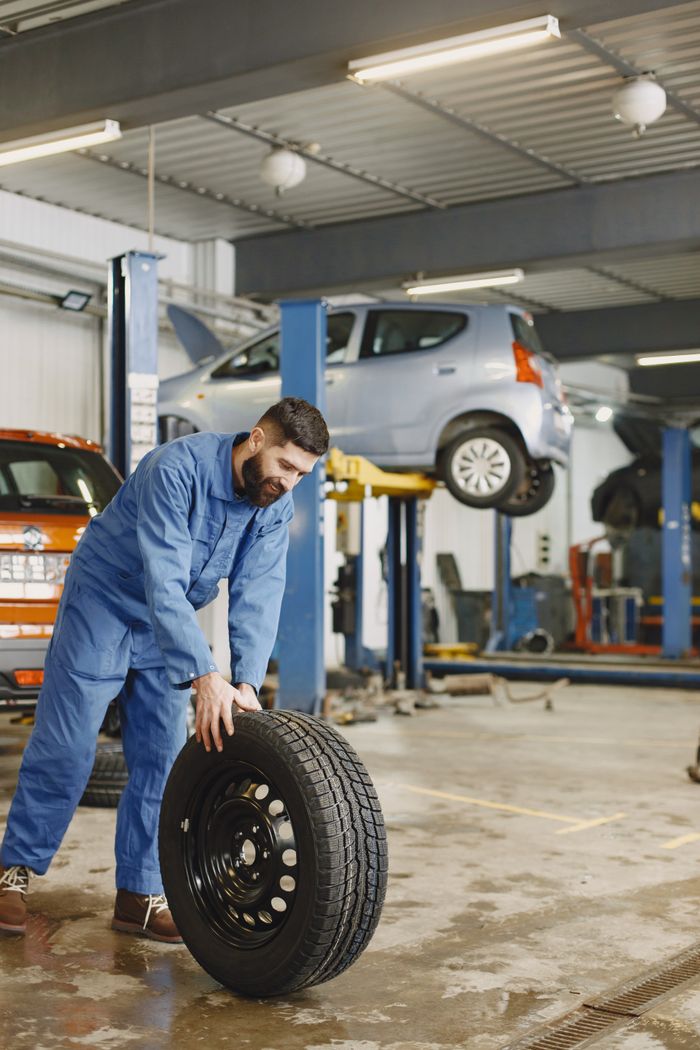 About Mechanic handling a tire in a busy automotive repair workshop.
