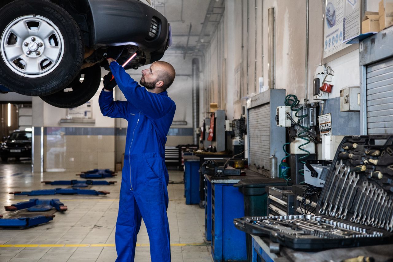 About Mechanic inspecting a raised car in an auto workshop for maintenance and repair services.